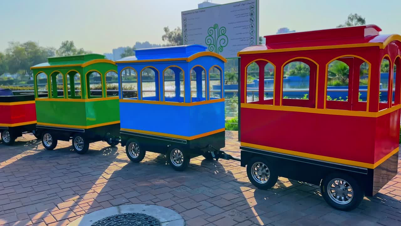 Vibrant 4K footage of a small colorful park train with red, blue, and green carriages shining in sunlight. Ideal for family, children, leisure, and transportation themes.