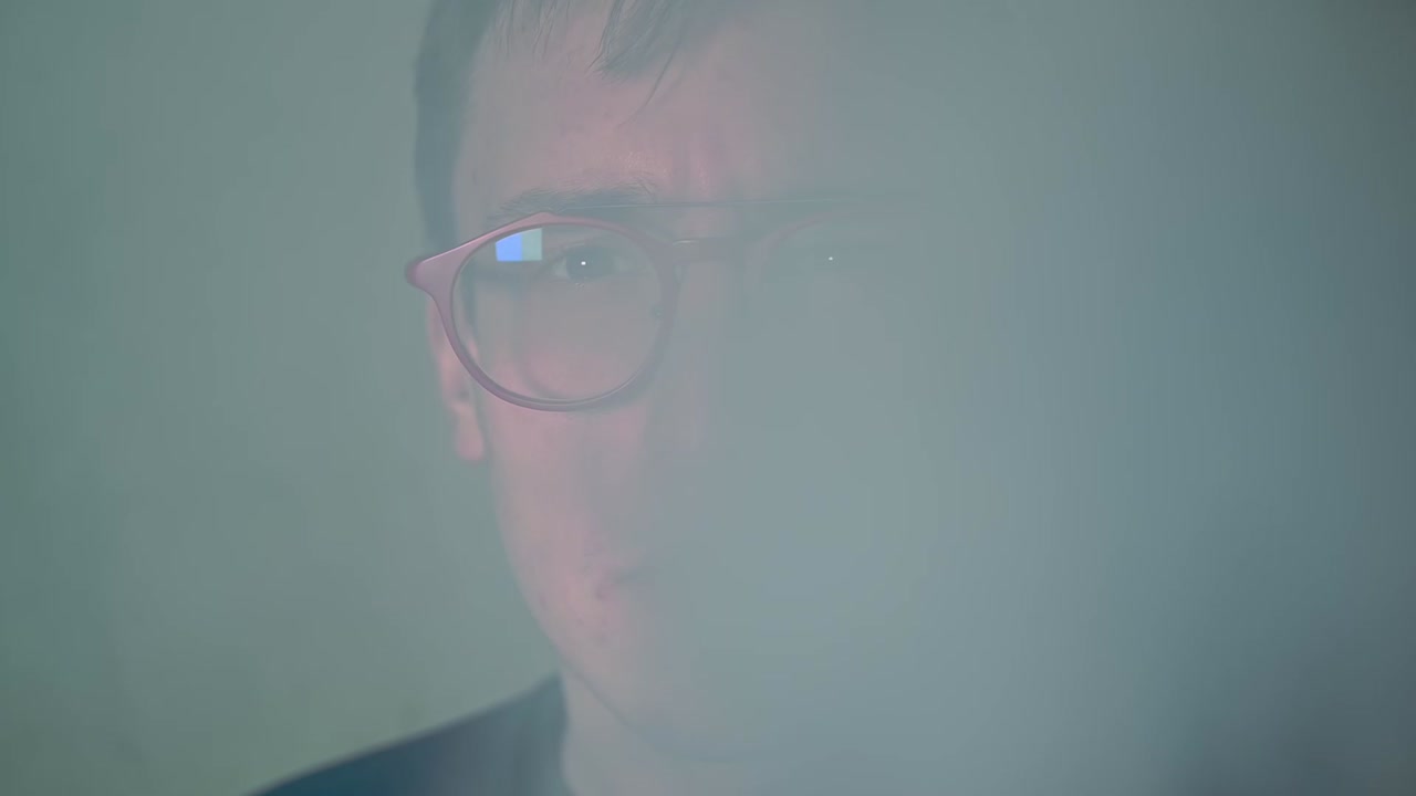 Young high man with red glasses vaping and exhales smoke in the camera. Smiling at the end. Close up. Slow motion