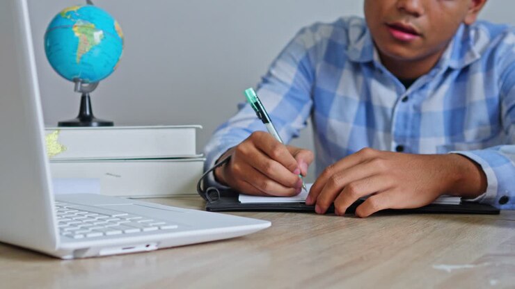 Male student writing in notebook at desk
