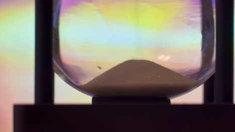 Closeup-time-hourglass-on-table,-sand-flowing-through-the-bulb-of-sandglass-on-purple-tone-template