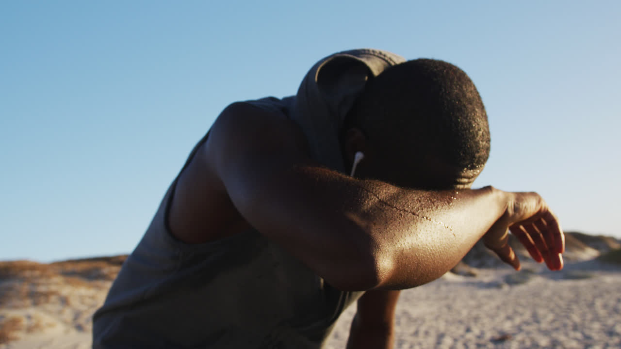 hombre afroamericano enfocado tomando un descanso en el ejercicio al aire libre junto a la playa