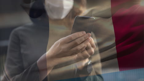 bandera francesa ondeando contra una mujer que usa una máscara facial usando un teléfono inteligente
