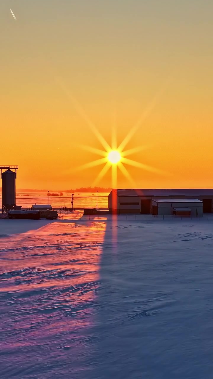 Eine filmische Luftaufnahme einer industriellen Landwirtschaftsanlage und Getreidesilos während eines lebhaften Sonnenuntergangs in der goldenen Stunde mit schneebedecktem Boden