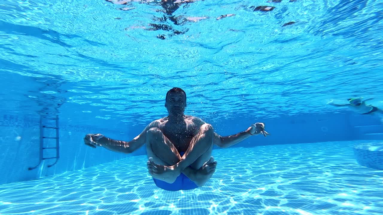 Man sitting underwater in yoga pose. Underwater view inside the swimming pool of a healthy man doing exercise. Underwater sport.