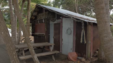 Holztisch-Und-Stühle-Vor-Dem-Alten-Barackenhaus-Aus-Welldach-Am-Strand