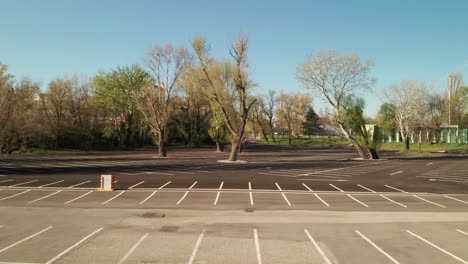empty parking lot with trees during the covid-19 pandemic. aerial ascending tilt reveal shot revealing the parking lot.
