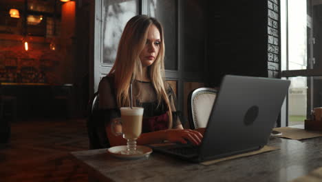 Portrait-of-a-young-girl-she-works-as-a-freelancer-in-a-cafe-drinking-a-delicious-hot-Cup-of-coffee-from-text-send-mail