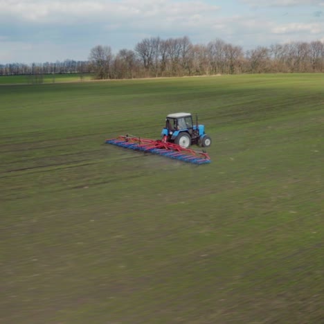 drone shot over tractor with harrow system plowing ground on cultivated farm field