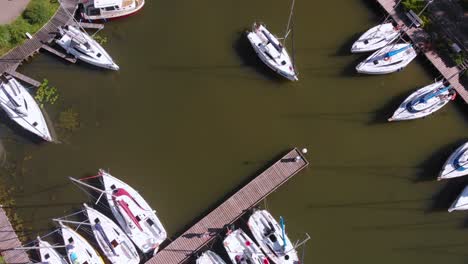 Aerial-shot-top-down-view-yacht-getting-out-of-small-marina-with-some-yacht-moored
