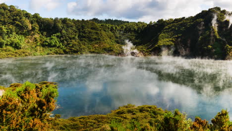 panning shot of boiling volcanic lake in national park of new zealand - epic green mountains and clear lake during sunlight - toxic sulfur steam rising up