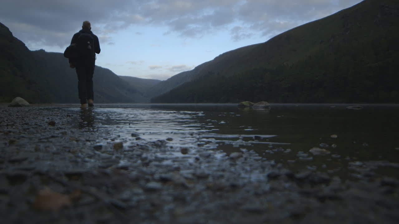 Un escursionista cammina nell'acqua lungo un bellissimo lago a Wicklow, Irlanda.