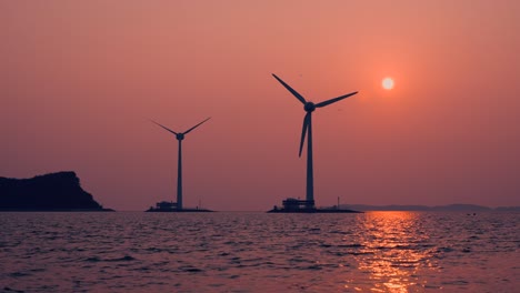 spinning windmill or wind turbine at tando port in ansan during pink sunset over sea and nueseom island in silhouette - static low angle