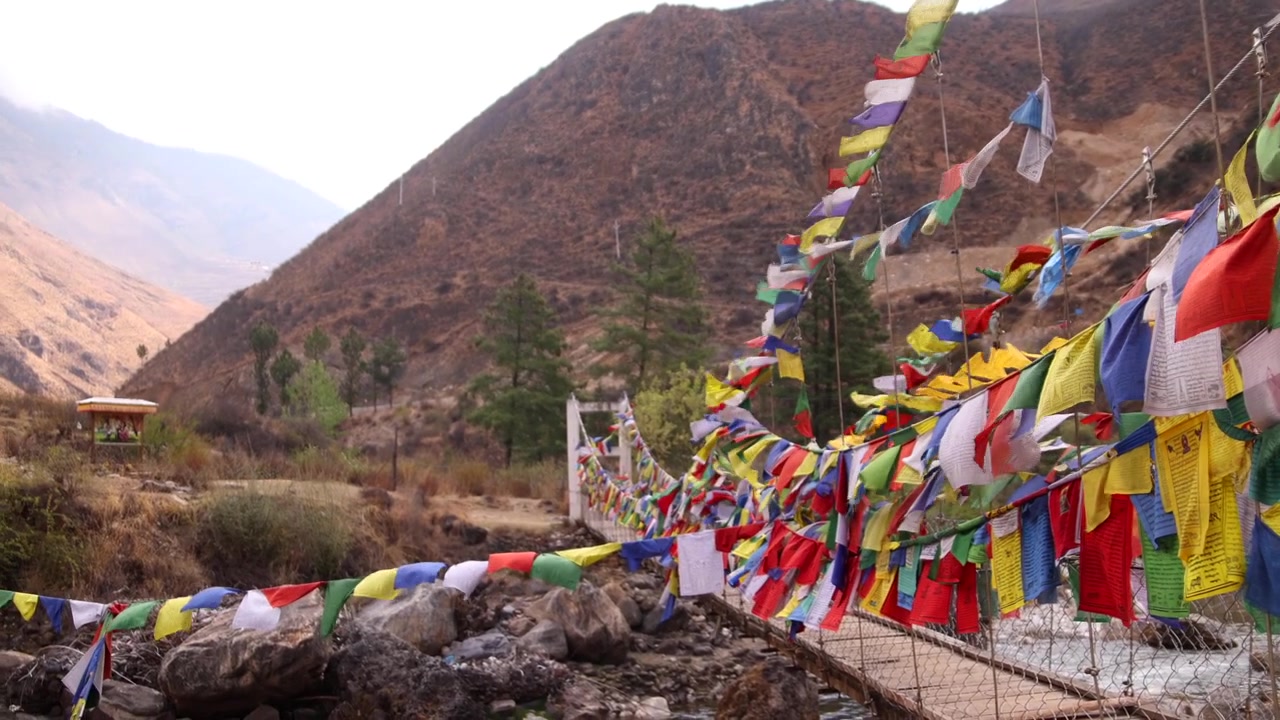 Rækker af buddhistiske bedeflag blafrer langs en flodbro i de bhutanske bjerge
