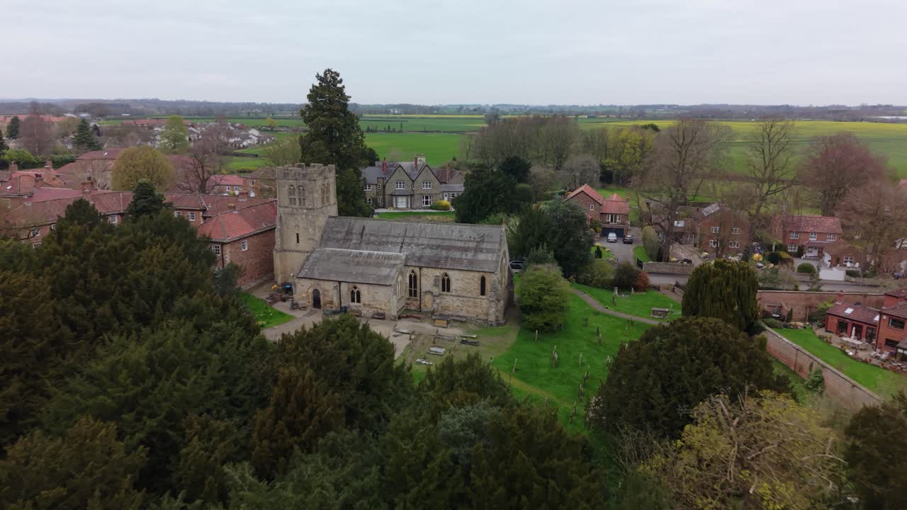 Smuk droneoptagelse fra luften, der afslører en historisk Church of England-bygning på landet i Yorkshire i en fredelig landsby på en overskyet dag