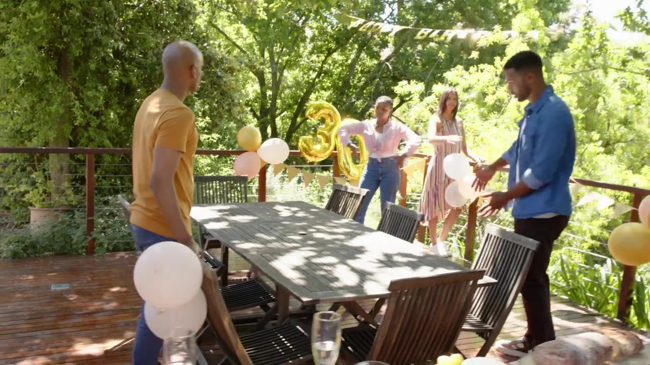 Approaching wooden table, group of four placing chairs and securing gold 30 balloons for birthday