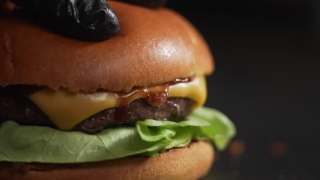 hand of the chef in black rubber gloves pressing burger with cheese and sauce in slow motion