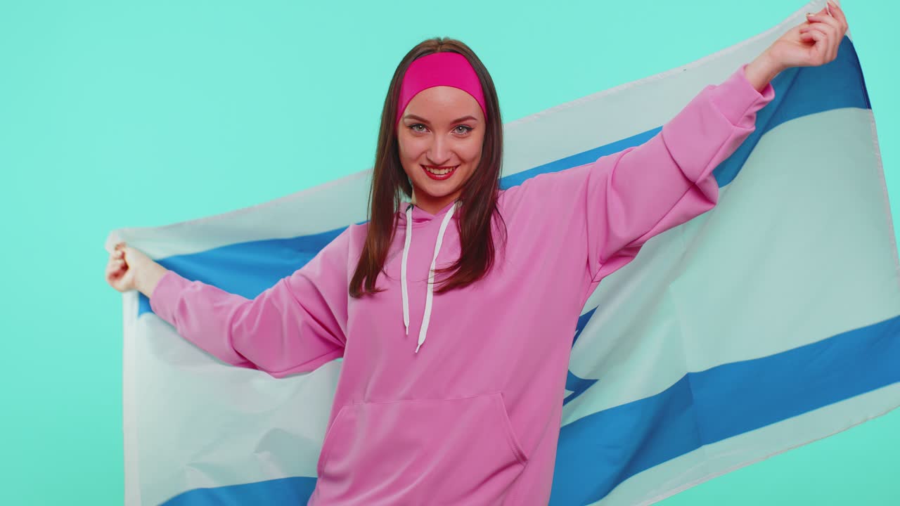 Cheerful lovely teen girl waving and wrapping in israel national flag celebrating independence day