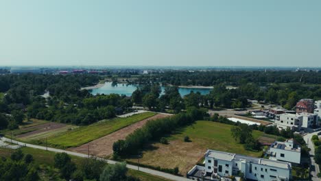 aerial - lake jarun and zagreb’s outskirts with houses and forest under bright summer skies