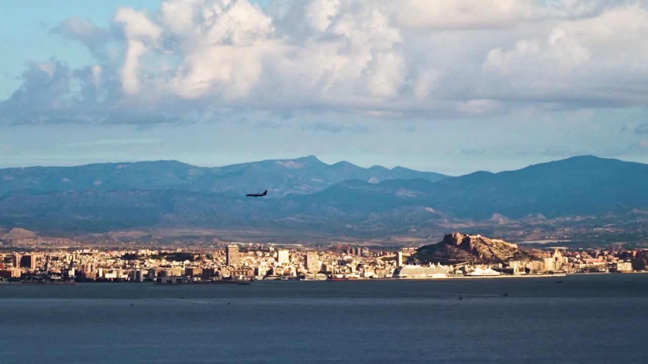한 마을 이 물 건너편 에서 볼 수 있다 - 앞면 에 비행기 가 날아가고, 멀리서 배 가 떠다니고 있다