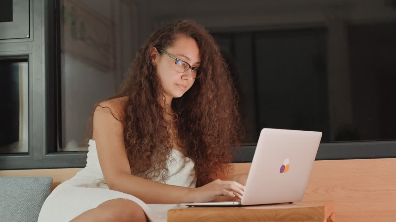 Quiet hotel room with focused female employee. Late evening scenes of woman working on her laptop at hotel. Woman remains focused on her laptop late into night in peaceful hotel room