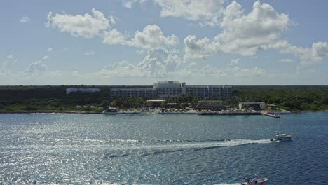 cozumel mexico aerial v2 drone fly away from fiesta americana contemporary resort overlooking at caribbean sea, with two speed boats cruising in the foreground with water wakes - september 2020
