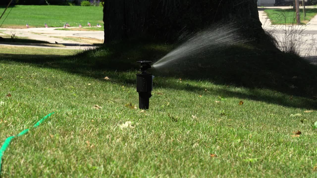 Long shot of a sprinkler head opening up and turning on to water a lawn
