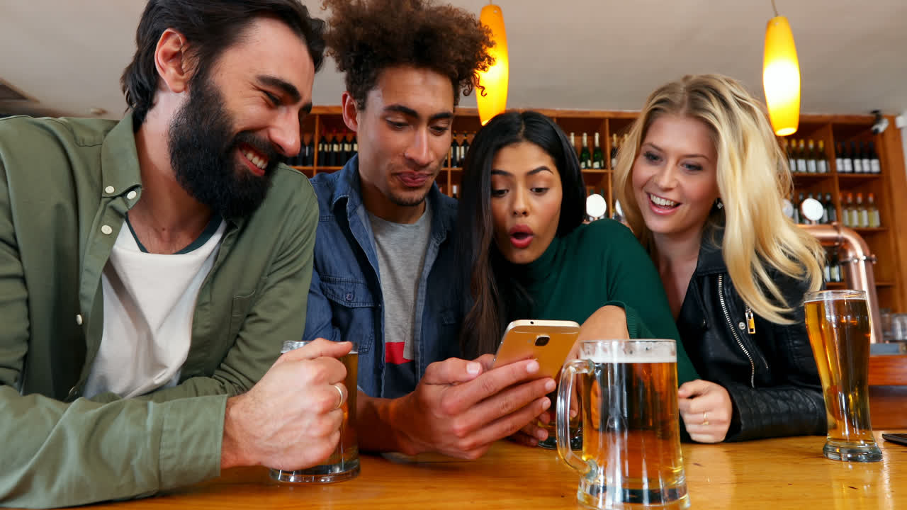 amigos felices usando el teléfono móvil mientras tienen un vaso de cerveza 4k