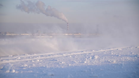 snowy landscape with industrial factory in the distance during a blizzard