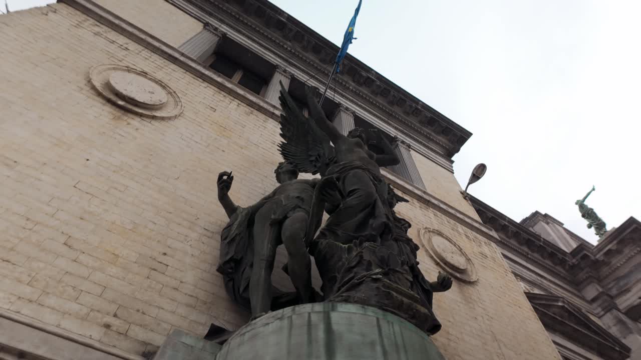 Low-angle view of a bronze sculpture group featuring a winged figure on a stone facade. Historic architectural detail and monument in the city center of Brussels, Belgium