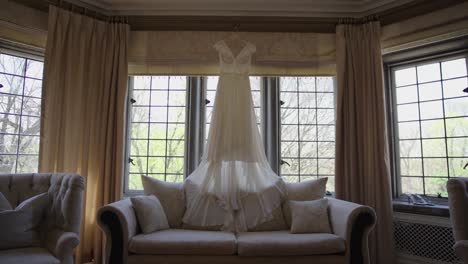 backlit wedding dress hanging in mansion house window above ornate stylish sofa