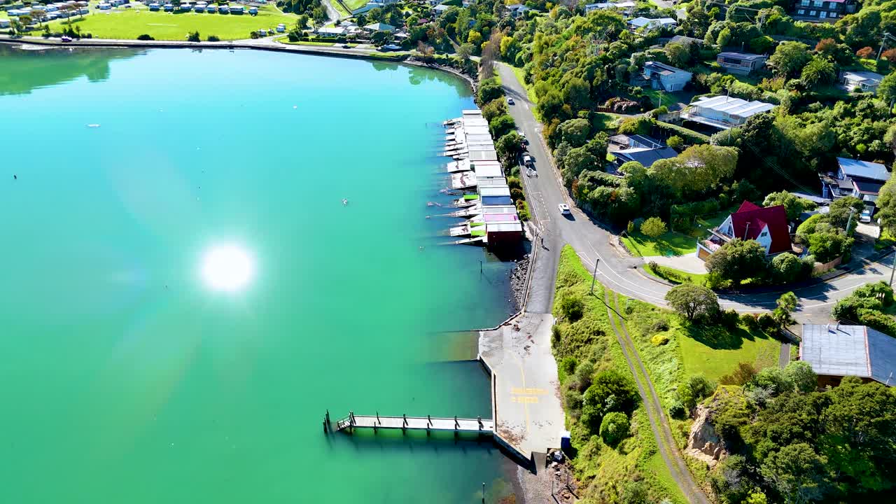 Aerial footage captures Akaroa's vibrant harbor, lush greenery, and rolling hills under bright sunlight, showcasing serene natural beauty