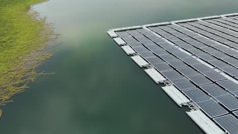 Drone fly over floating solar panels installed on the surface of a lake in Sungai Rawang, Serendah, Malaysia. The large grid of photovoltaic panels rests on buoyant structures, bordered by calm water