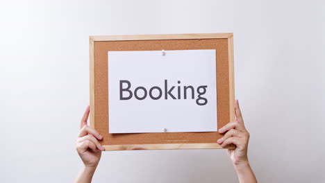 woman's hand shows the paper on board with the word booking in white studio background with copy space