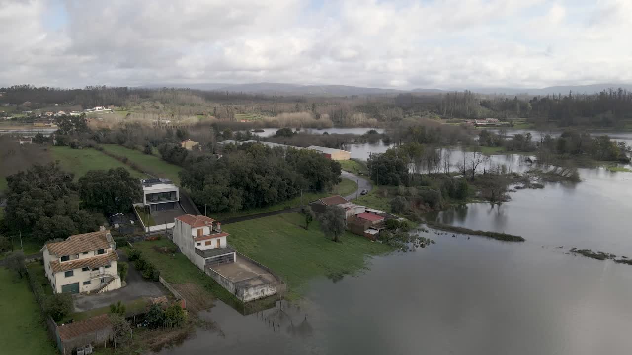Ampio panorama aereo che mostra terreni agricoli allagati che si estendono per tutta la valle, con zone di terreno più elevato che emergono dalla linea di galleggiamento. Drone che avanza sopra le rive del fiume e le case.