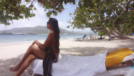 young adult latin woman stands up from shaded area to walk on beach, playa teco maimon