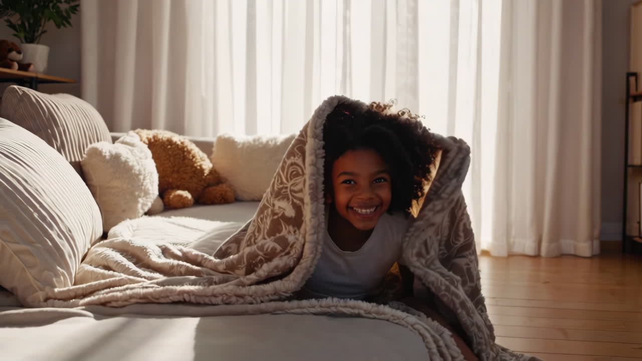 Joyful little girl playing under a cozy blanket on a bed