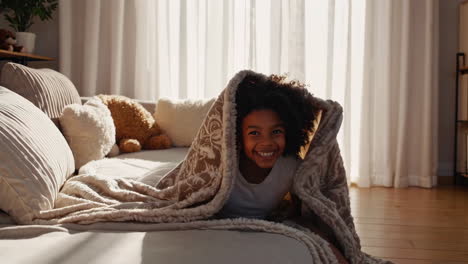 joyful little girl playing under a cozy blanket on a bed