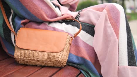 woman sitting on a bench wearing a striped sweater and pink skirt with a straw bag