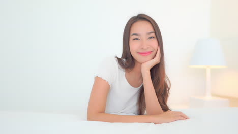 portrait of young beautiful satisfied asian woman on bed smiling to camera, full frame