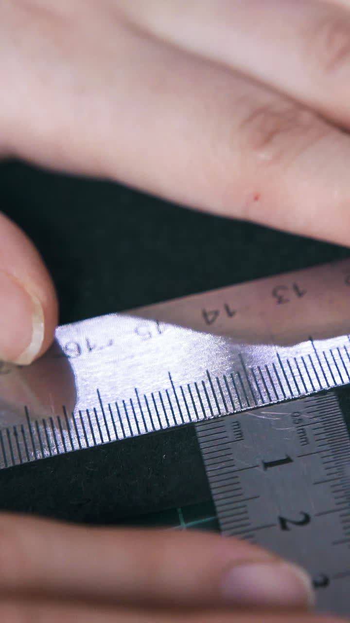 CU: Tailor measures black leather cloth with large metal rulers on special green cutting mat extreme close view