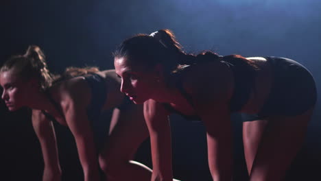 three girls in black clothes are in the starting pads to start the race in the competition in the light of the lights and run towards the finish