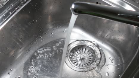 water stream from metal kitchen sink faucet draining in the sinkhole close up shot