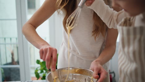 mom daughter kneading dough in bowl indoors close up. laughing woman mixing