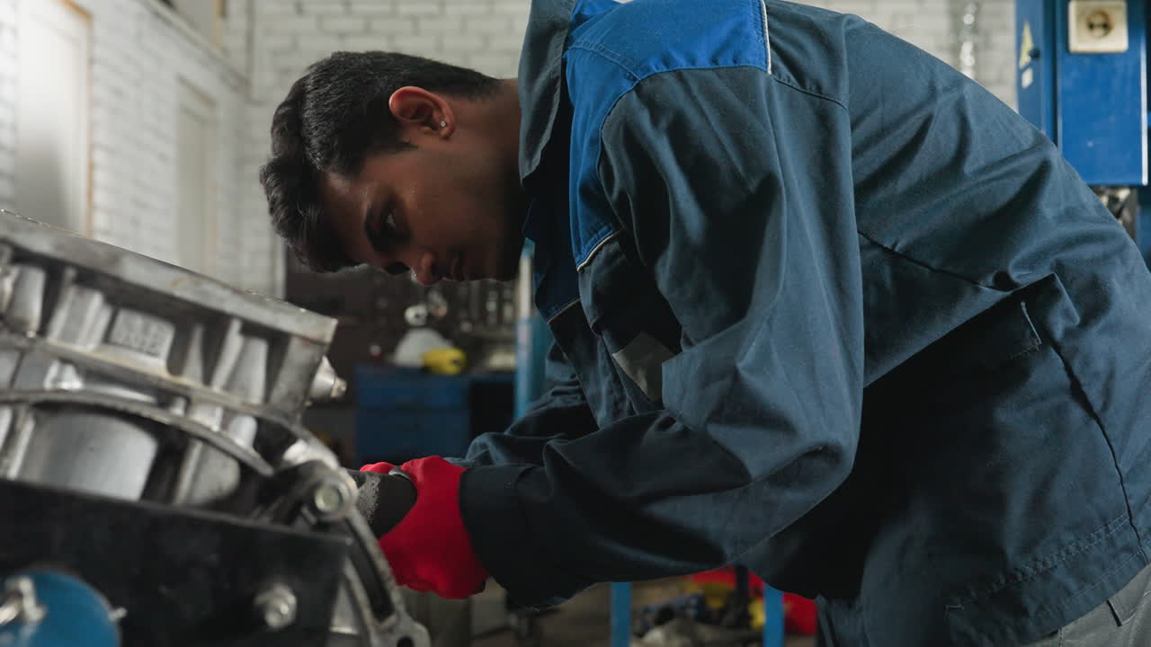 mecánico con guantes rojos utiliza herramienta neumática en el bloque del motor en el taller industrial, realizando reparaciones mecánicas precisas, trabajador enfocado en uniforme azul ajusta los componentes del motor