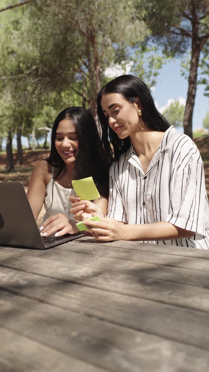 dos mujeres trabajando en una computadora portátil al aire libre