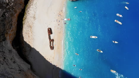 Aerial:-Top-down-view-of-yacht-and-sailboats-floating-on-the-coast-of-Navagio-beach-in-Zakynthos-Greece