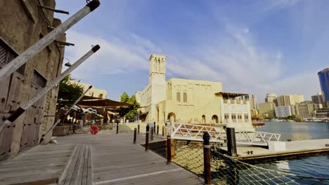 Walking-On-Wooden-Promenade-In-Al-Seef-With-Cityscape-Background-Near-Al-Fahidi,-Dubai-UAE