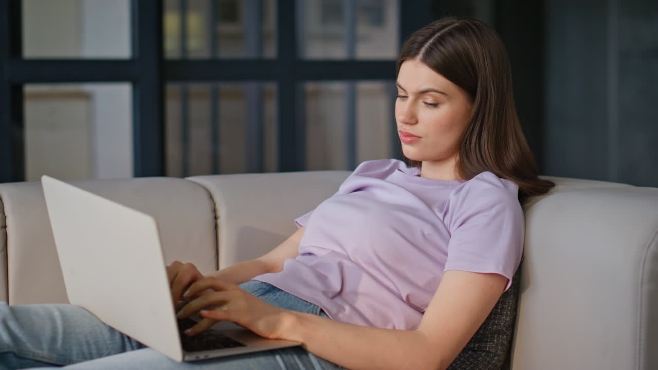 Focused freelancer working laptop lying comfortable sofa closeup. Woman texting