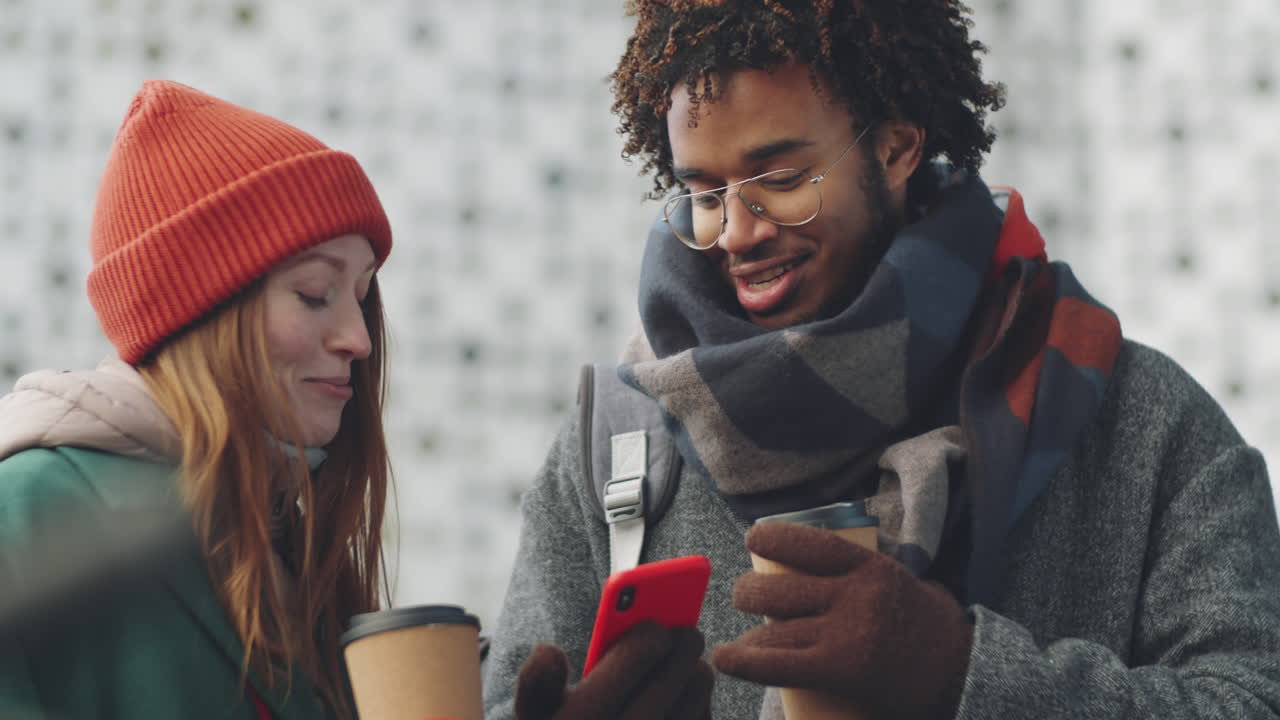 pareja disfrutando de café y usando un teléfono inteligente al aire libre en invierno