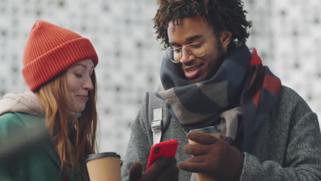 couple enjoying coffee and using a smartphone outdoors in winter